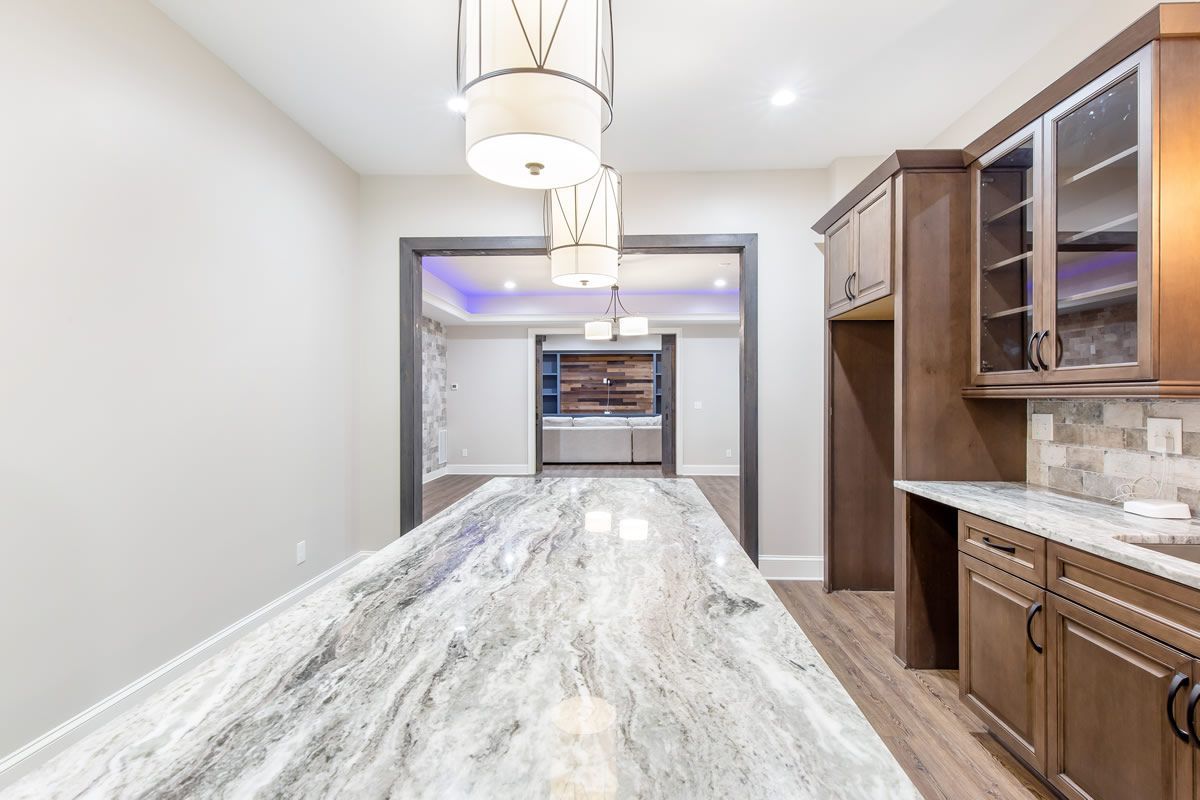 Kitchen with marble countertop, wood cabinets, and pendant lights; doorway in the background.