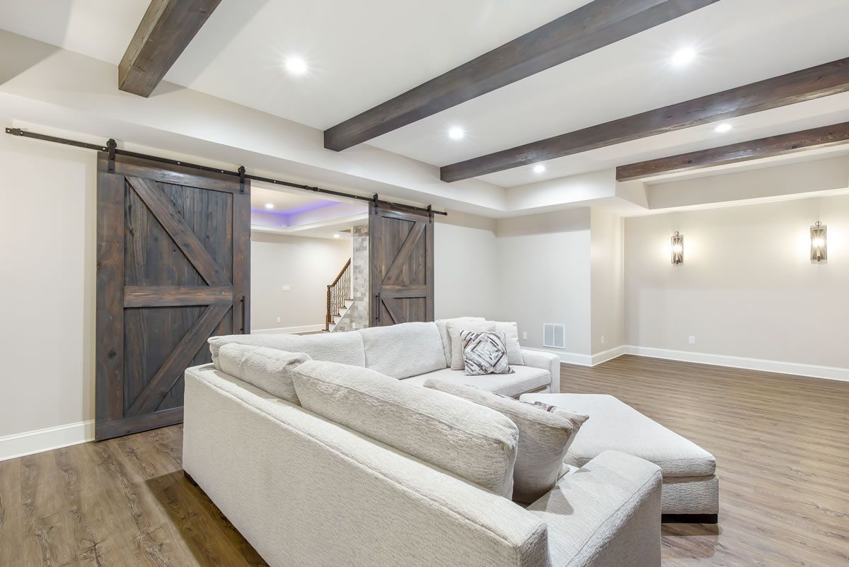 A modern living room with a white sectional sofa, barn doors, and wood beams.