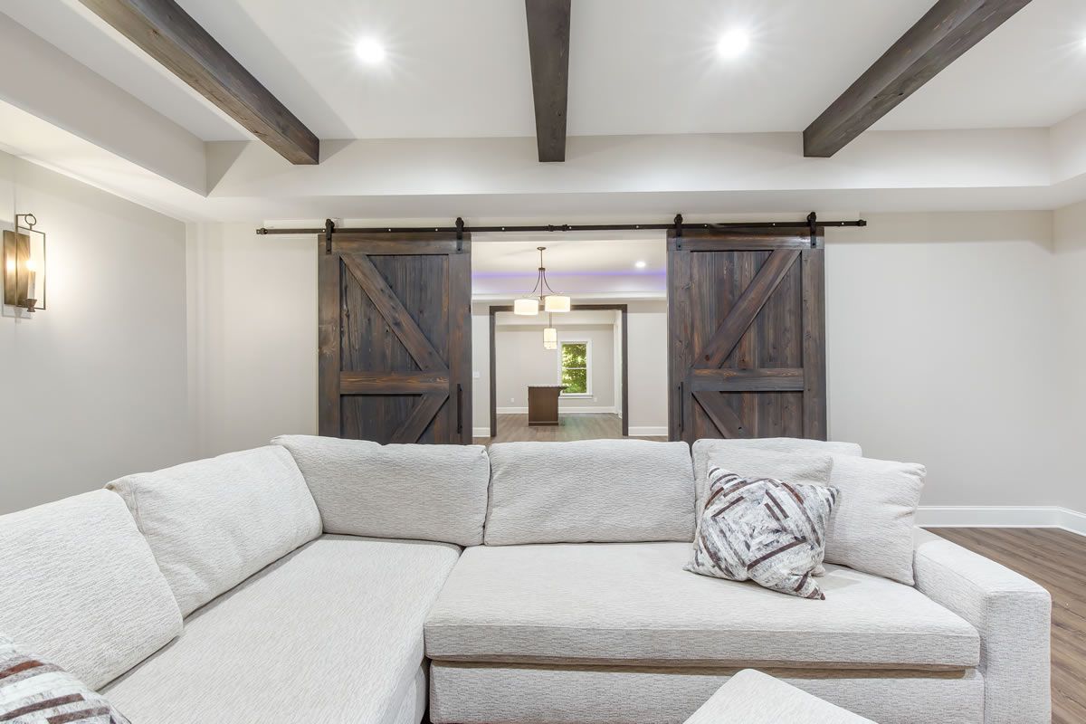 Cozy living room with light-colored sectional, dark barn doors, and exposed wooden beams.