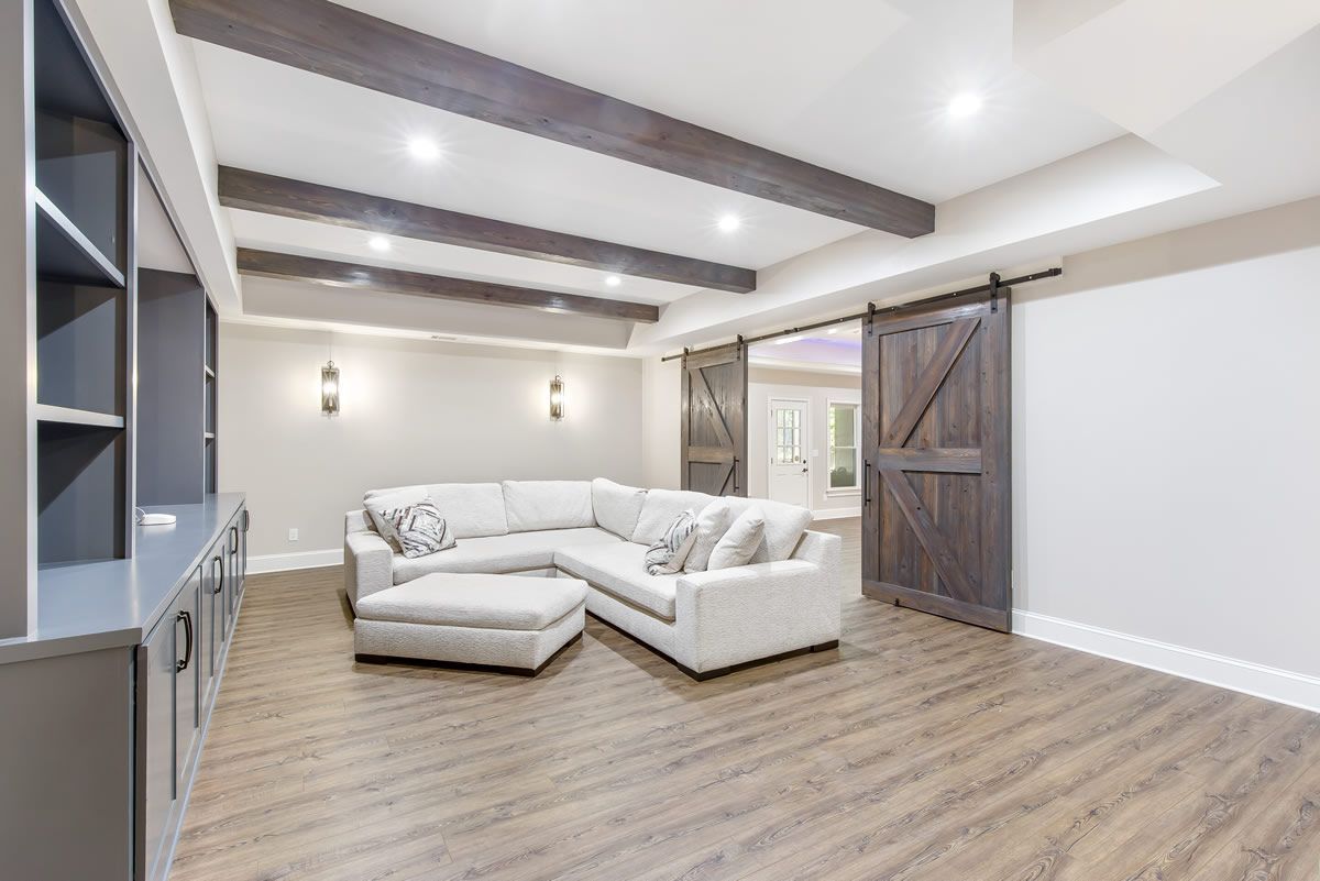 Living room with sectional sofa, built-in shelving, wooden beams, barn door, and wood-look flooring.