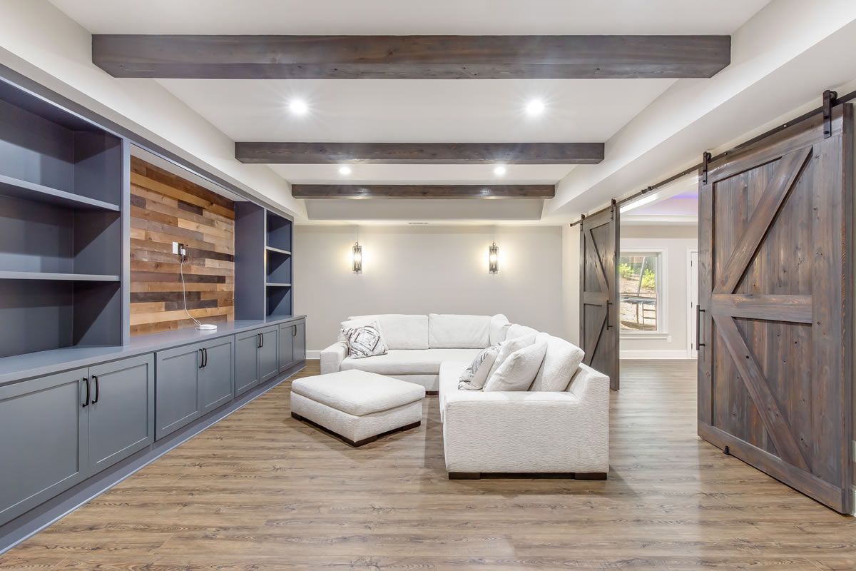 Cozy finished basement with built-in cabinetry, sectional sofa, barn doors, and wood-look flooring.