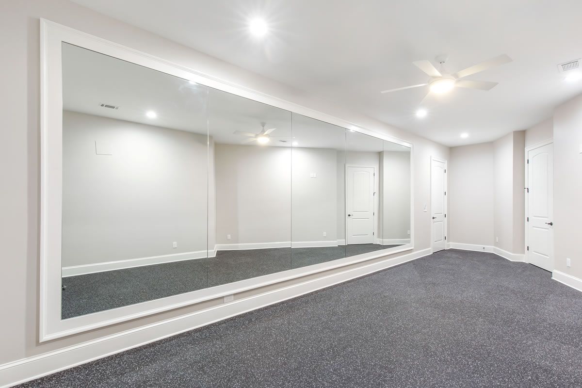Large room with a wall-sized mirror, gray carpet, white walls and ceiling, recessed lighting, and a ceiling fan.