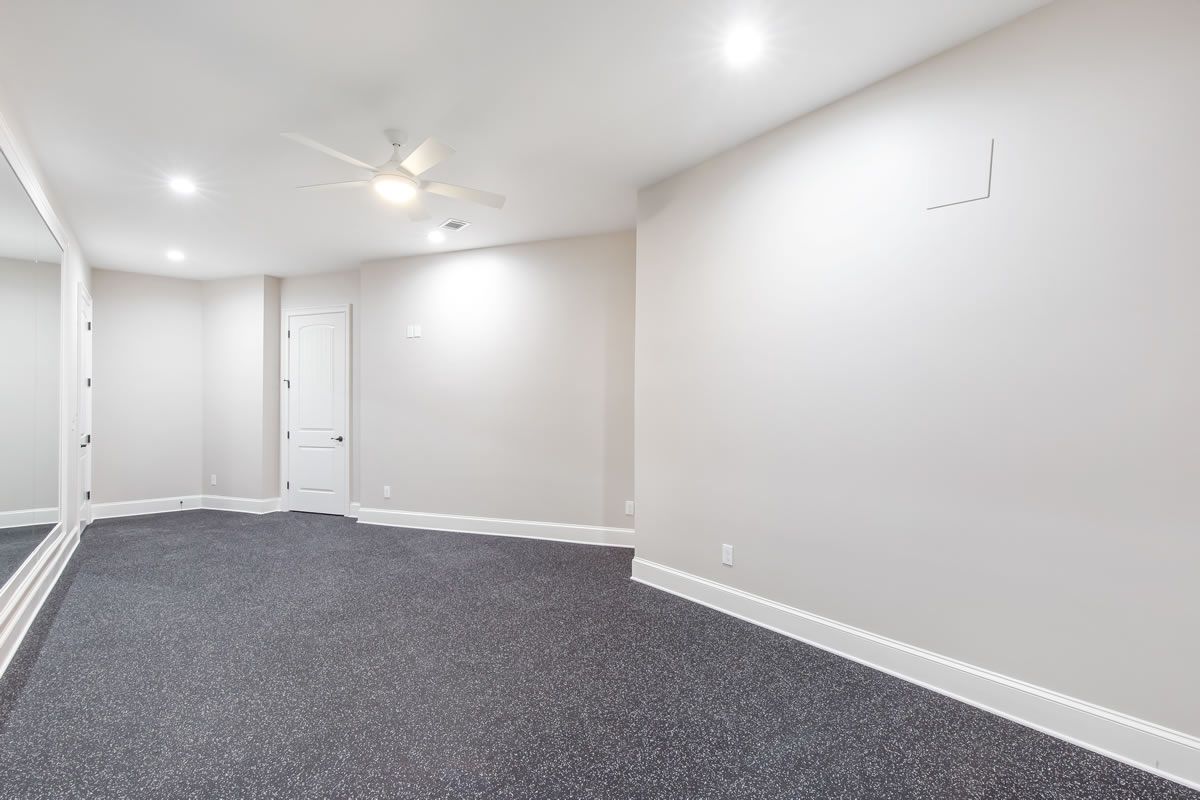 Empty room with gray carpet, white walls, mirror, and ceiling fan.