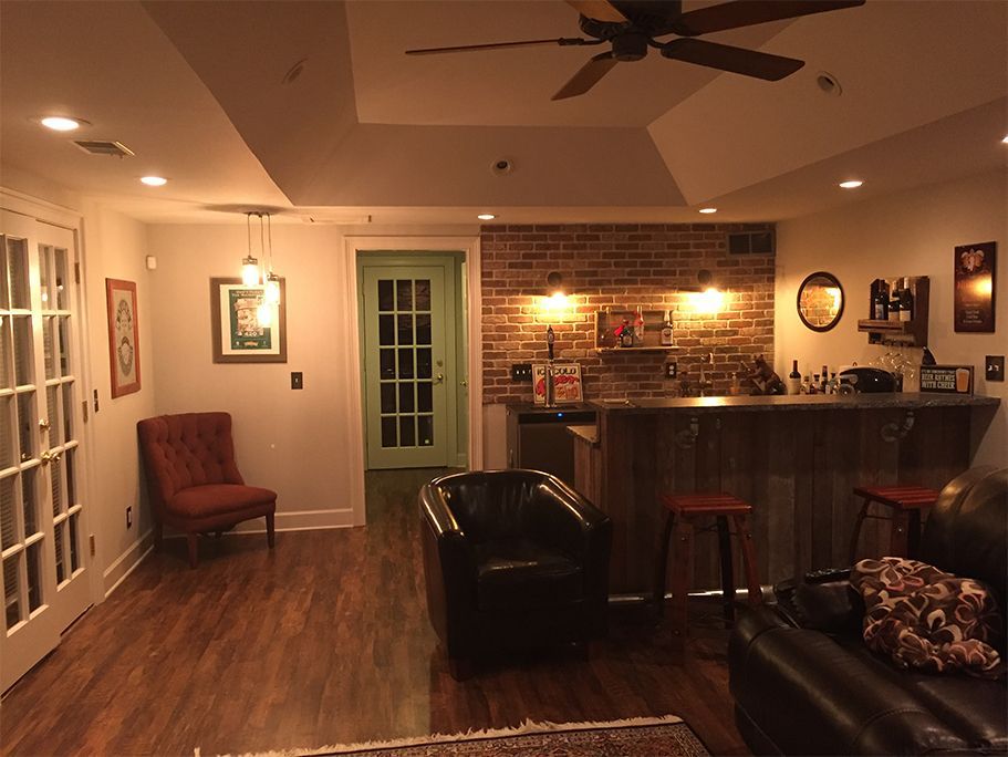 Cozy basement living area with bar, exposed brick, dark wood floors, and leather seating.