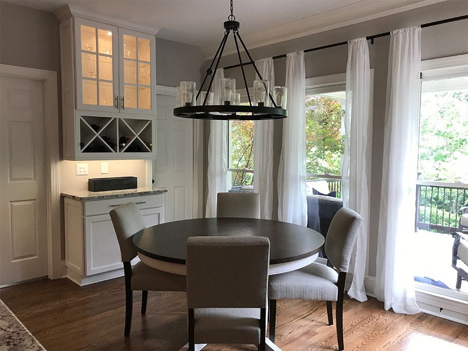 Dining room with round table, chairs, chandelier, and windows with white curtains.