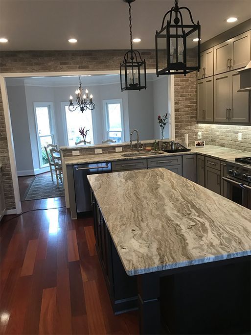 Kitchen with gray cabinets, granite countertops, and a large island with a patterned countertop. Brick accent wall.