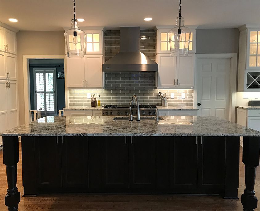 Kitchen with white and dark cabinets, granite island, stainless steel hood, and pendant lights.