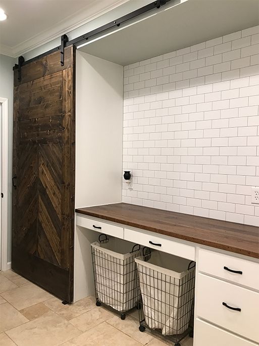 Laundry room with a sliding barn door, white cabinets, brick tile, and a wooden countertop.