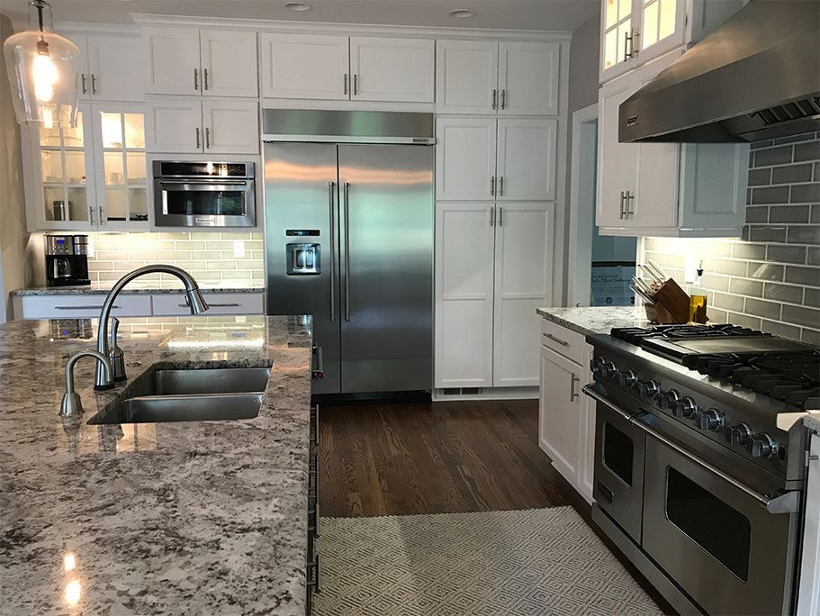 White kitchen with stainless steel appliances, granite countertops, and dark wood floors.