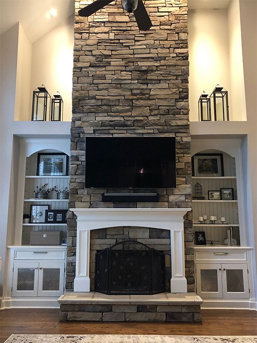 Stone fireplace with built-in bookshelves, TV, and black decorative lanterns in a living room.