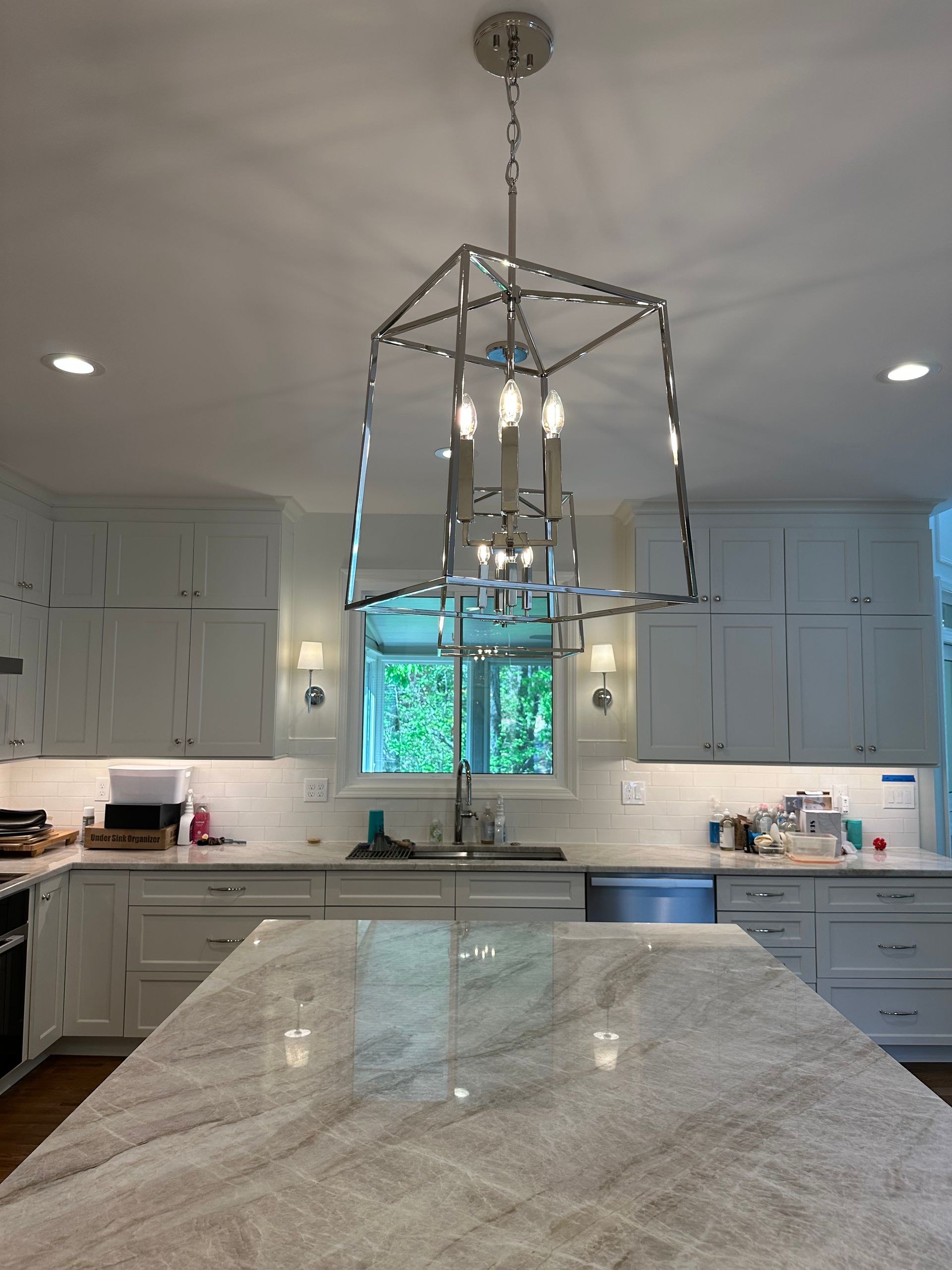 Kitchen with light blue and white color scheme; checkered floor, island with two stools, white cabinets.