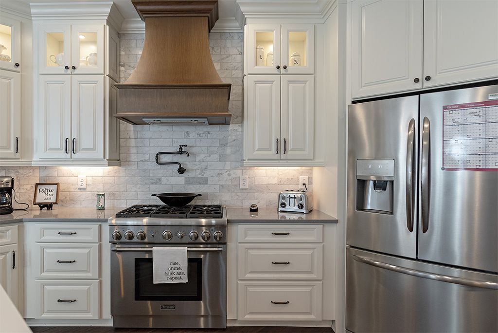 White kitchen with stainless steel appliances, marble backsplash, and wooden range hood.