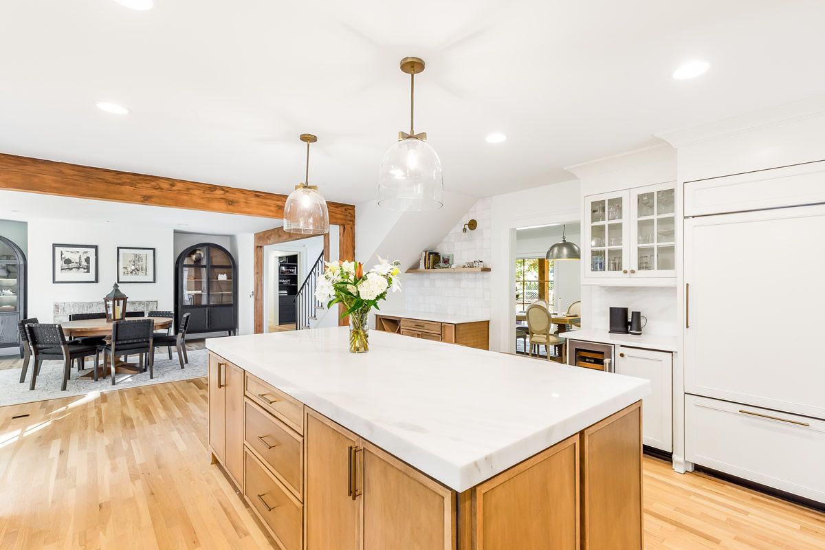 Open-concept kitchen with a large island and dining area. Wooden cabinets, white countertops, and light fixtures.