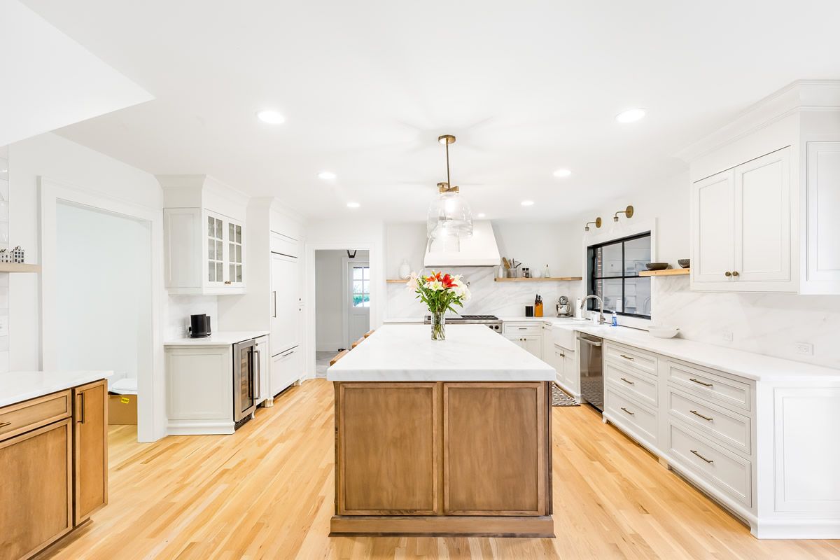 Bright kitchen with a large wooden island, white cabinets, and light wood flooring.