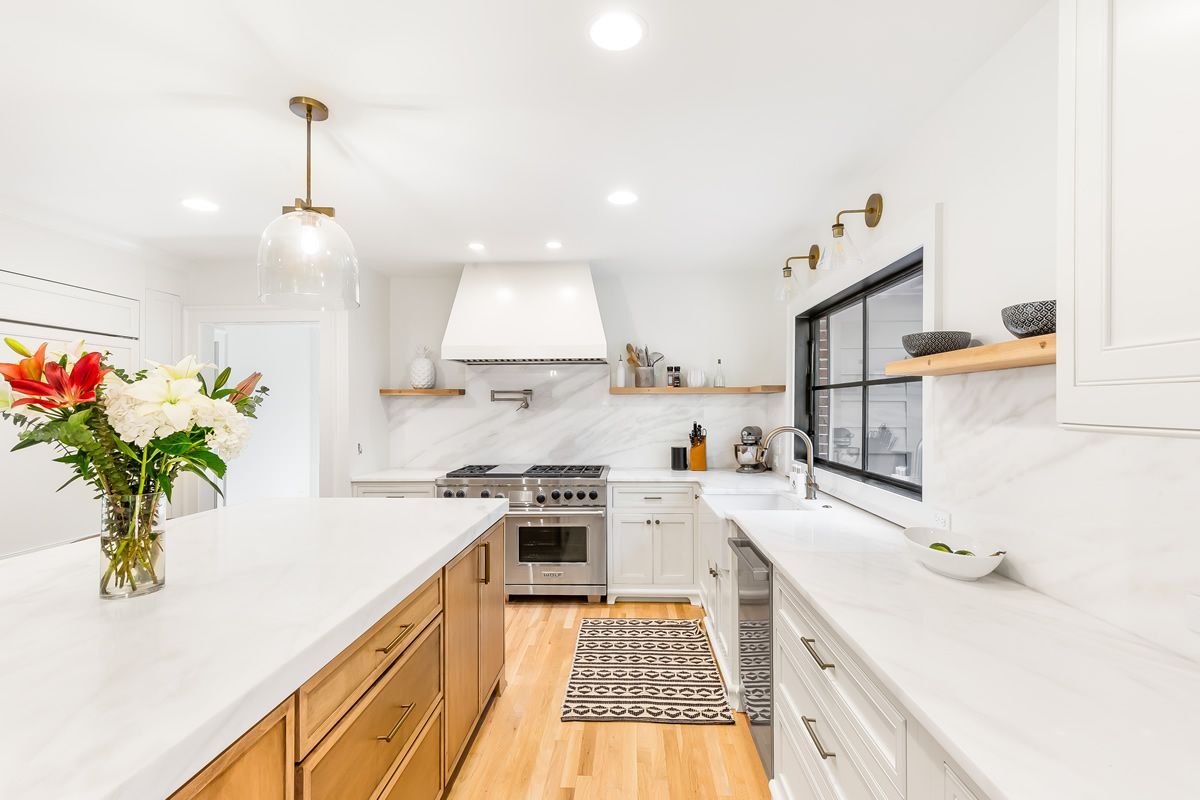 Bright white kitchen with a large island, stainless steel appliances, and wooden flooring.