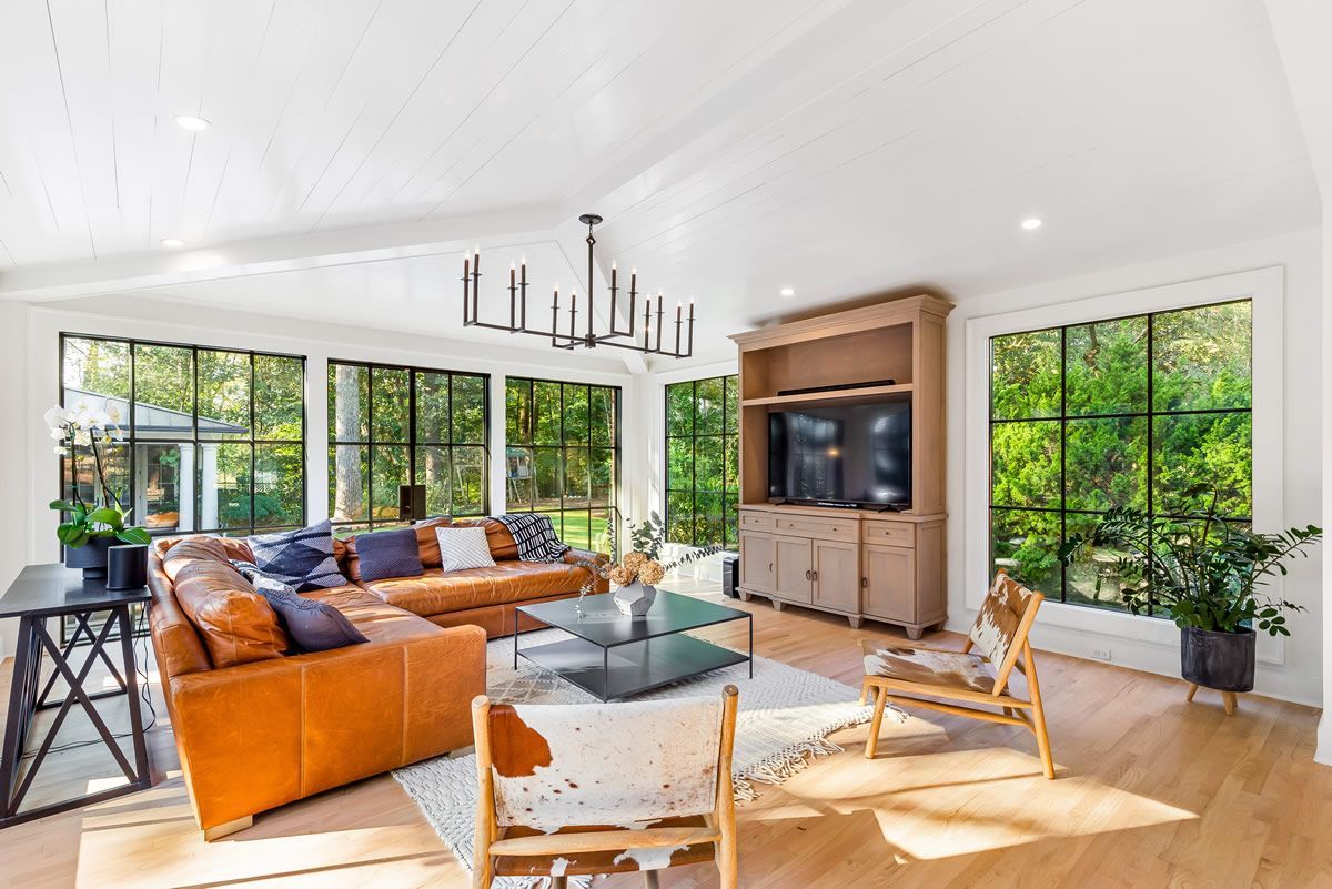 Living room with leather sofa, large windows overlooking greenery, and a built-in entertainment center.