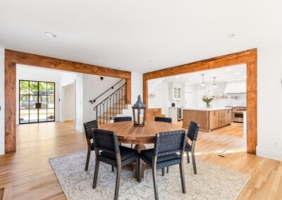 Dining room with a round wooden table and six black chairs, open to kitchen.