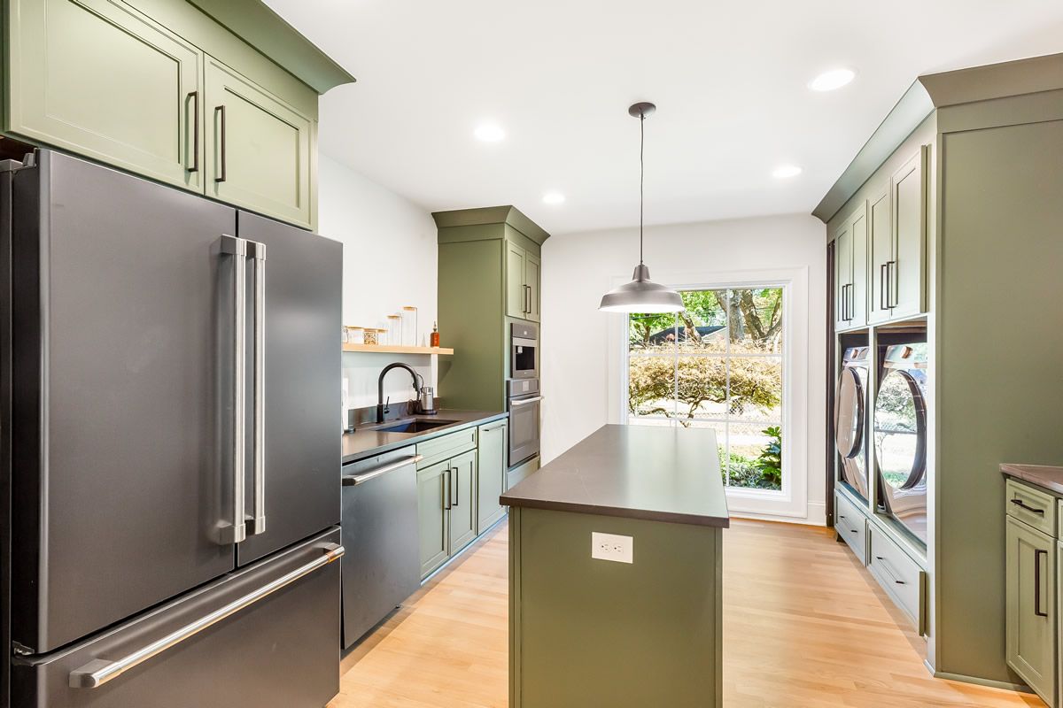 Green kitchen with black appliances, a central island, and a door to the outdoors.