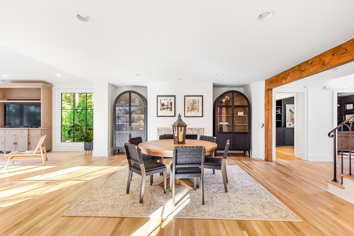 Spacious dining room with wooden floor, round table, and black chairs. Cabinets flank a fireplace.