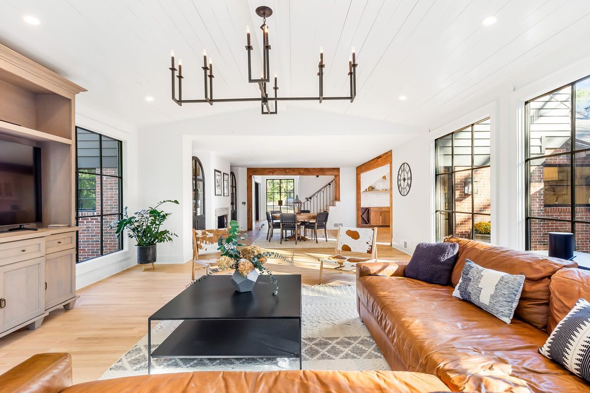 Living room with leather sofa, black coffee table, large windows, and chandelier.