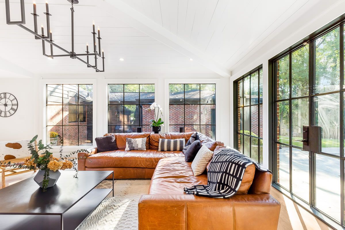 Living room with brown leather sectional, black framed windows, and a black chandelier.