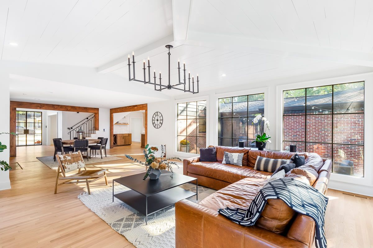 Spacious living room with leather sectional, black chandelier, and large windows.