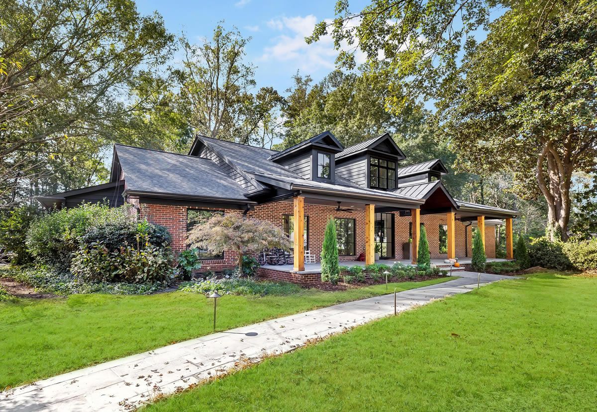 A brick and wood home with a covered porch sits on a grassy lawn with trees in the background.
