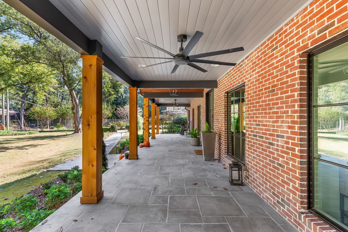 Covered brick patio with grey stone flooring, wooden support columns, and ceiling fans.