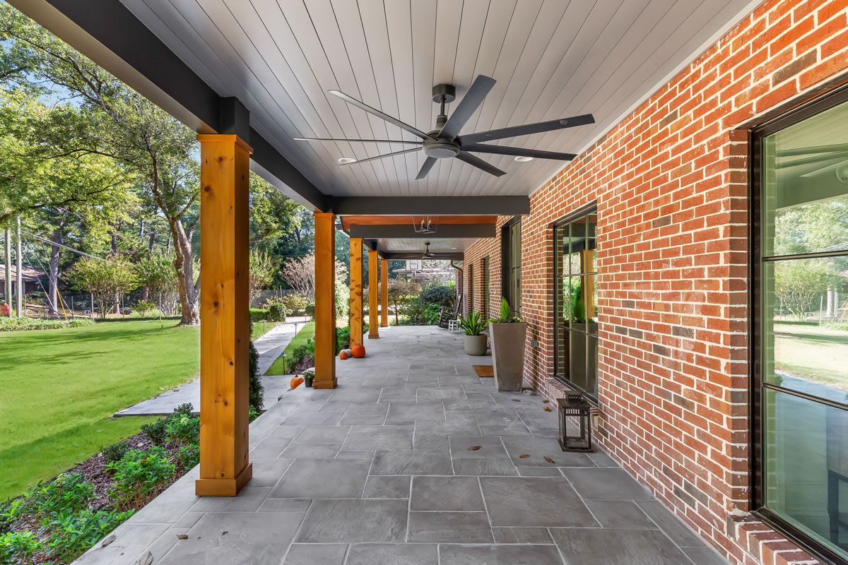 Covered porch with brick wall, stone floor, wooden posts, ceiling fans, and green lawn.