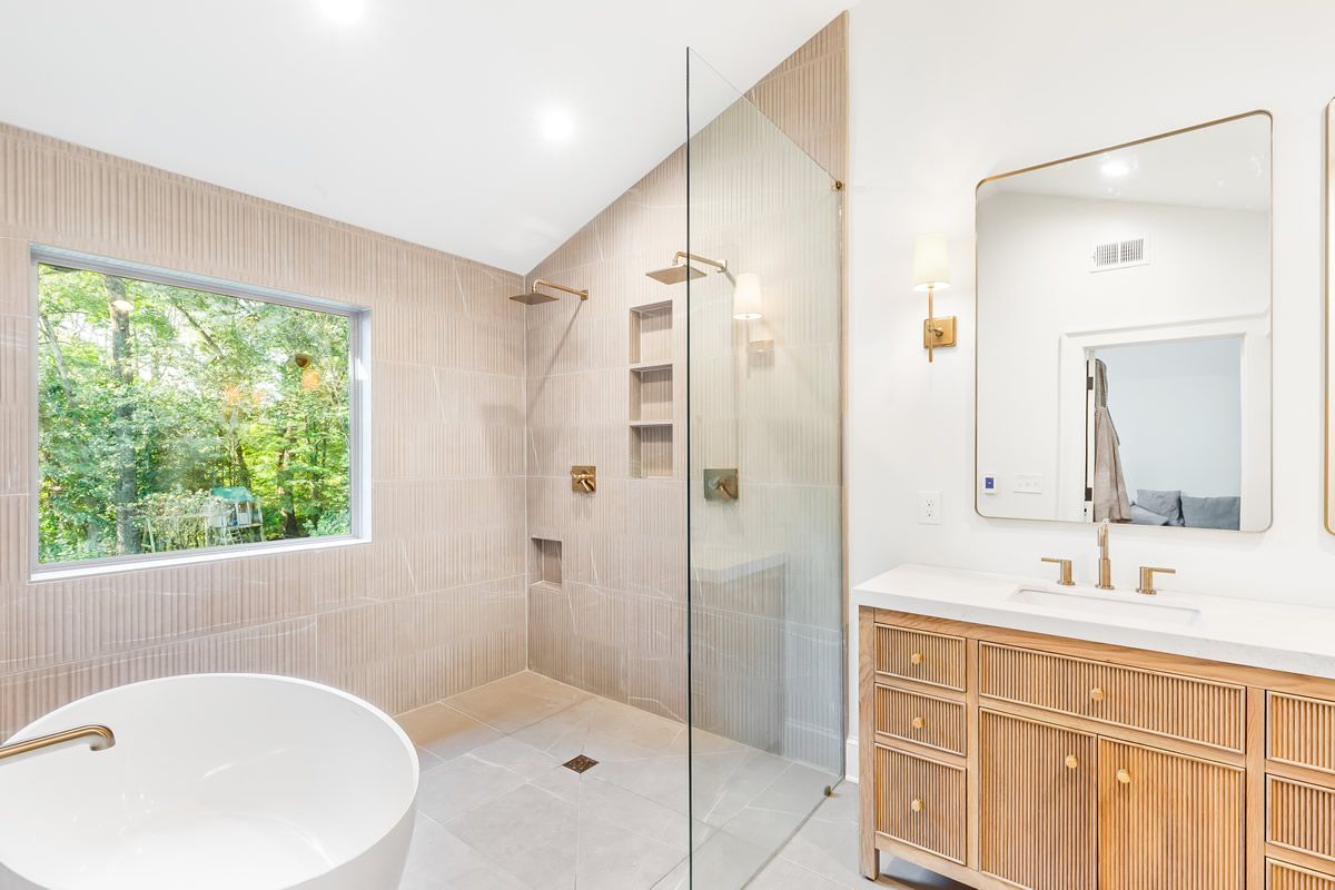 Modern bathroom with a walk-in shower, soaking tub, vanity, and window overlooking trees.