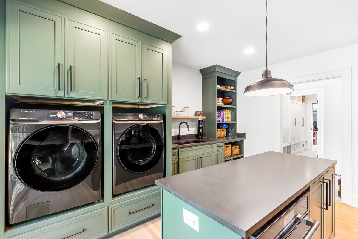 Laundry room with green cabinetry, black appliances, island, and overhead lighting.