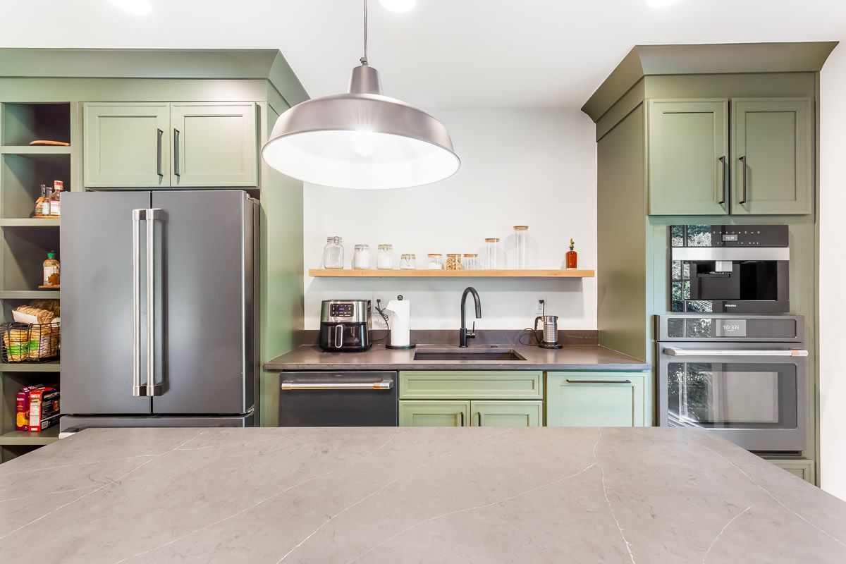 Green kitchen with a refrigerator, cabinets, countertops, and a pendant light.