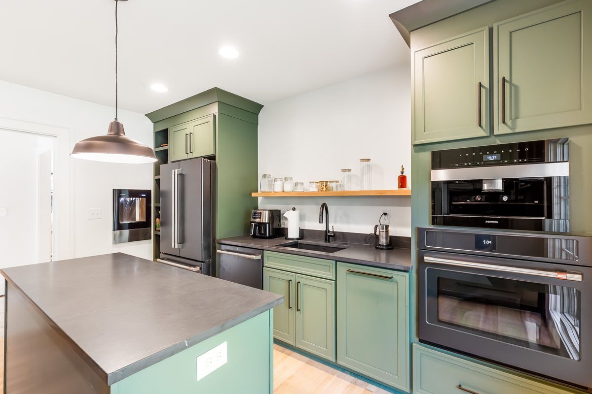 Green kitchen with island, black appliances, and wooden shelves.