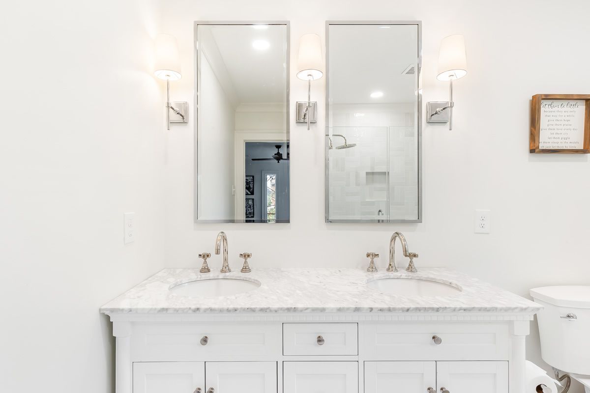 White bathroom with double vanity, mirrors, and sconces; marble countertop.