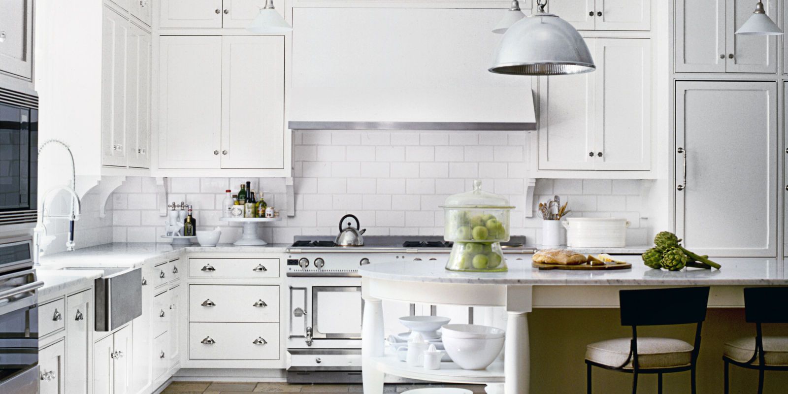 White kitchen with island, range, and cabinets. A large metal light hangs overhead.