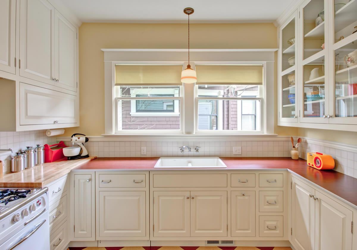 A white kitchen with red countertops, windows, and cabinets. A pendant light hangs above the sink.