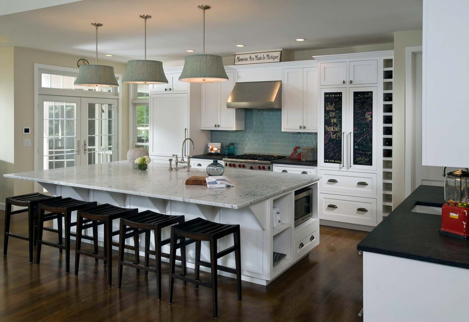 White kitchen with large island, pendant lights, stainless steel appliances, and dark stools.