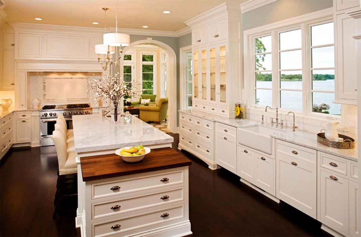 Elegant white kitchen with island, dark wood floors, and large windows with a scenic view.