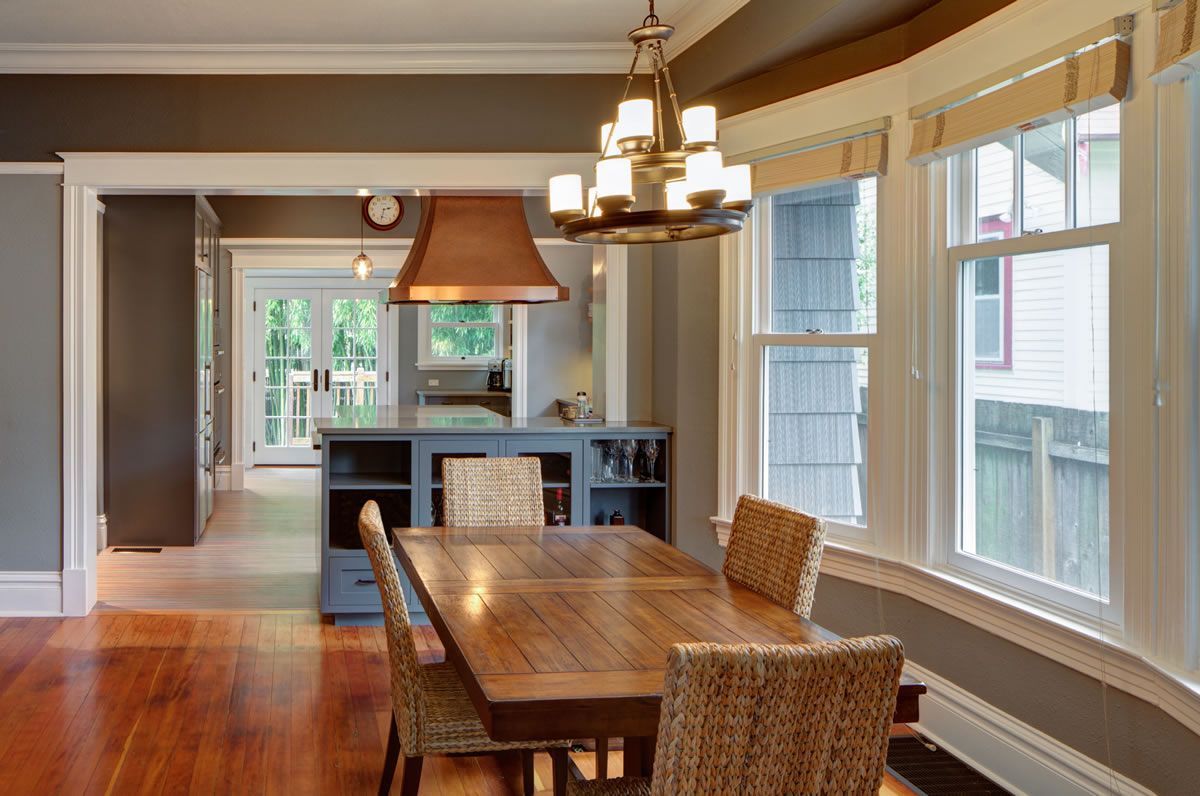 Dining room with wooden table, wicker chairs, chandelier, and a view into the kitchen.