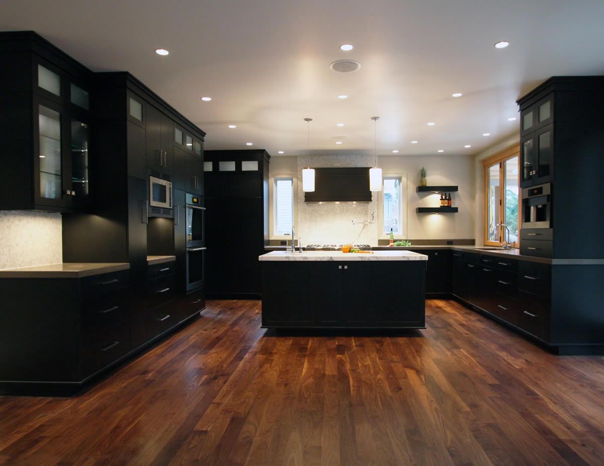 Dark kitchen with black cabinets, island, and wood floors. Recessed lighting.