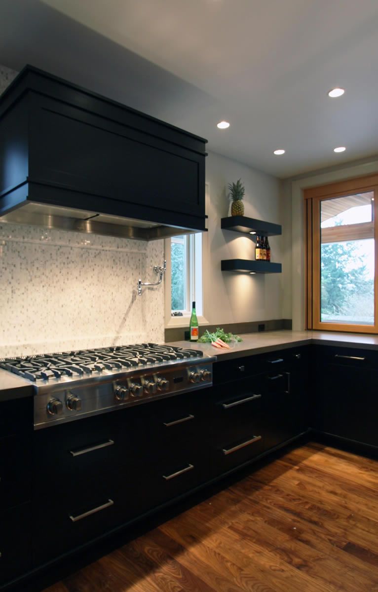 Modern kitchen with black cabinets, stainless steel range, and light countertops.