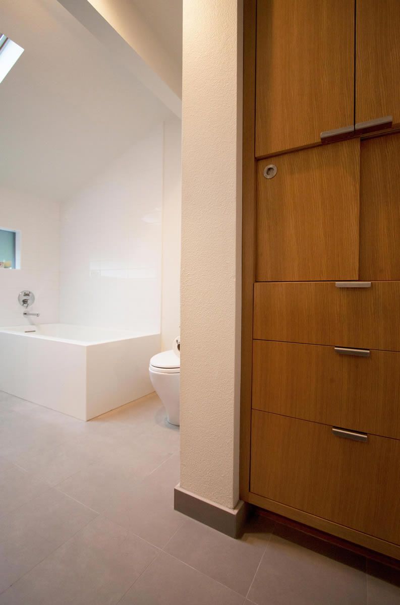 Bathroom with a white tub, toilet, and light gray floor. Wooden cabinet on the right.