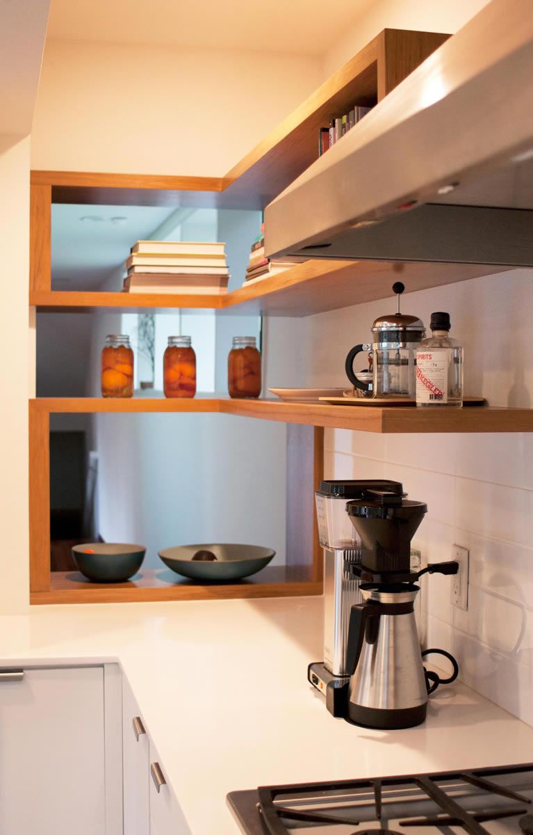 Kitchen corner with wooden shelves holding jars, bowls, and coffee equipment; white countertop.