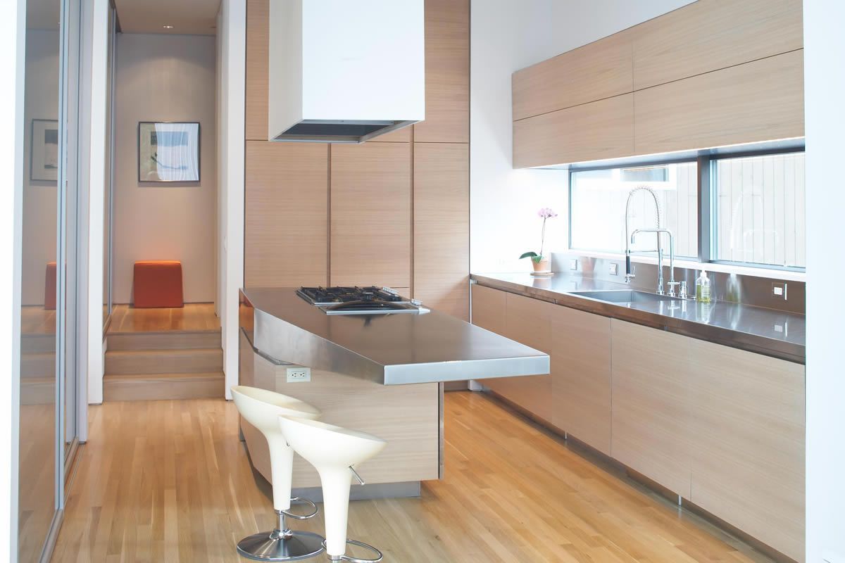 Modern kitchen with light wood cabinets, island with stovetop, and two bar stools.