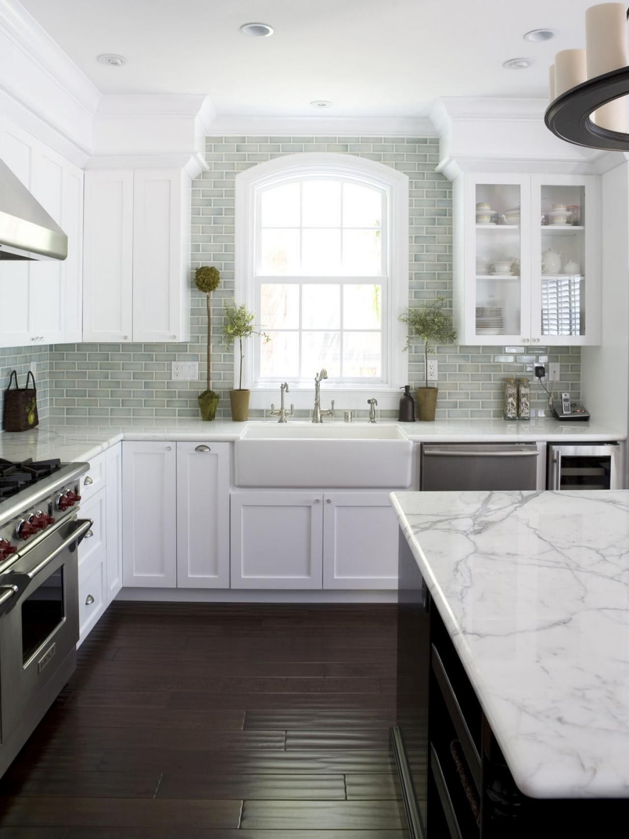 White kitchen with marble countertop island, dark wood floor, and green tile backsplash.