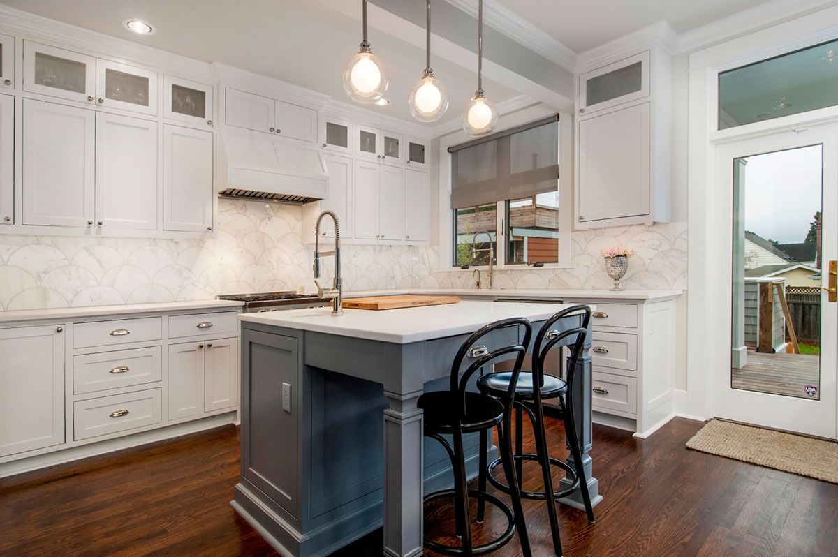 Bright white kitchen with gray island, dark wood floors, and black bar stools.
