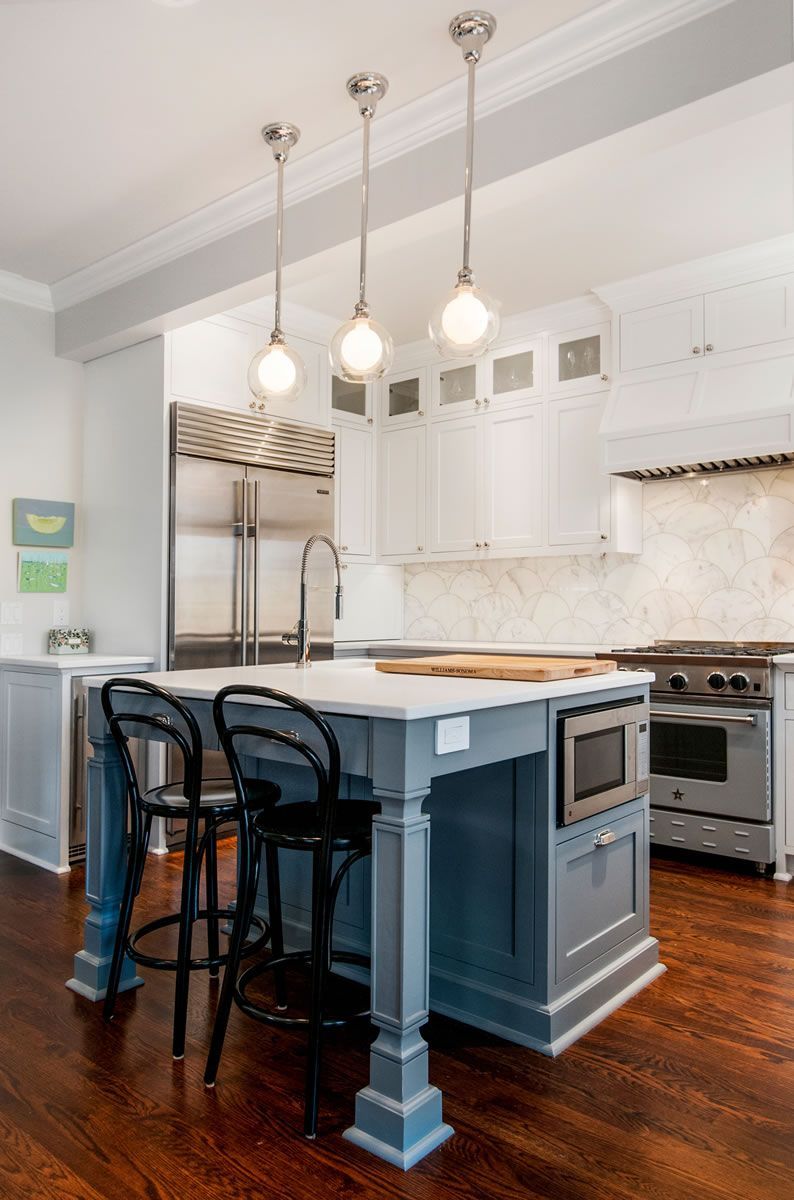 Kitchen with gray island, three pendant lights, stainless steel appliances, and dark wood floors.