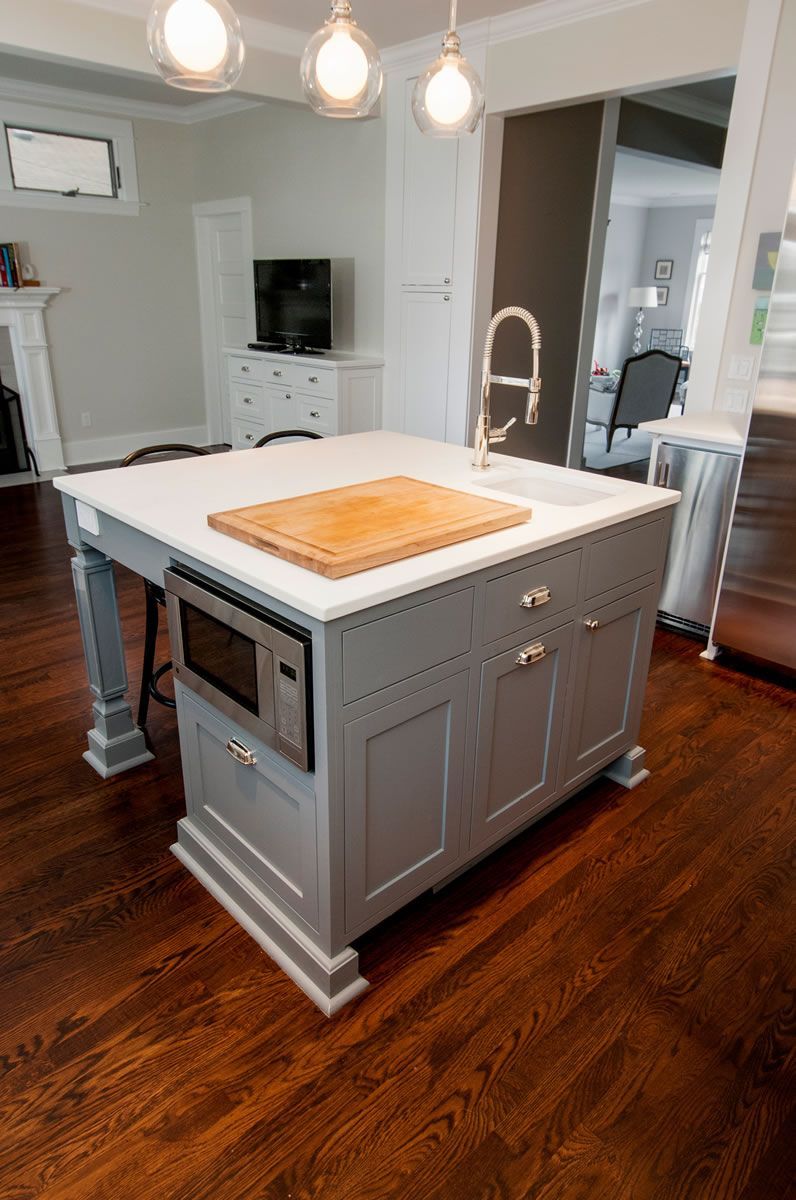 Kitchen island with a built-in microwave, sink, and cutting board on a wooden floor.