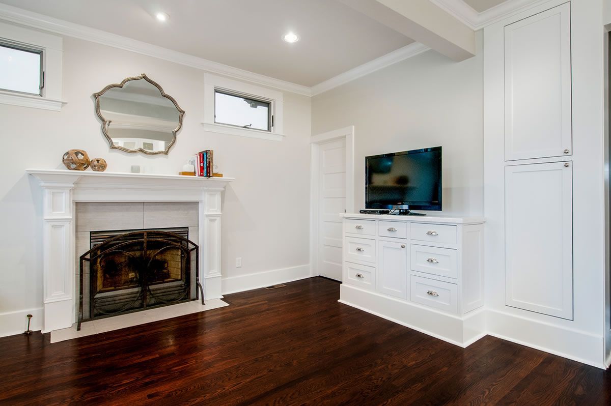 Cozy, white-walled room with a fireplace, TV on a cabinet, and dark wood floors.