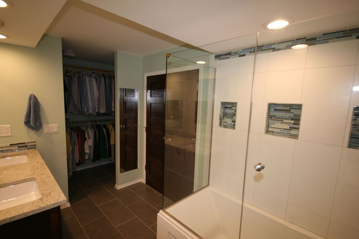Bathroom with shower, closet, and double vanity. Light blue walls, white and brown tiling, glass shower door.